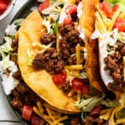 Ground beef tacos ready to eat topped with cheese, lettuce, sour crema, and tomatoes.