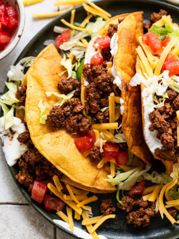 Ground beef tacos ready to eat topped with cheese, lettuce, sour crema, and tomatoes.