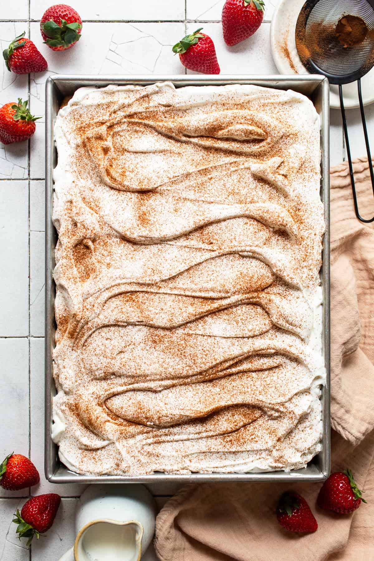 Tres leches cake recipe topped with whipped cream and garnished with ground cinnamon.