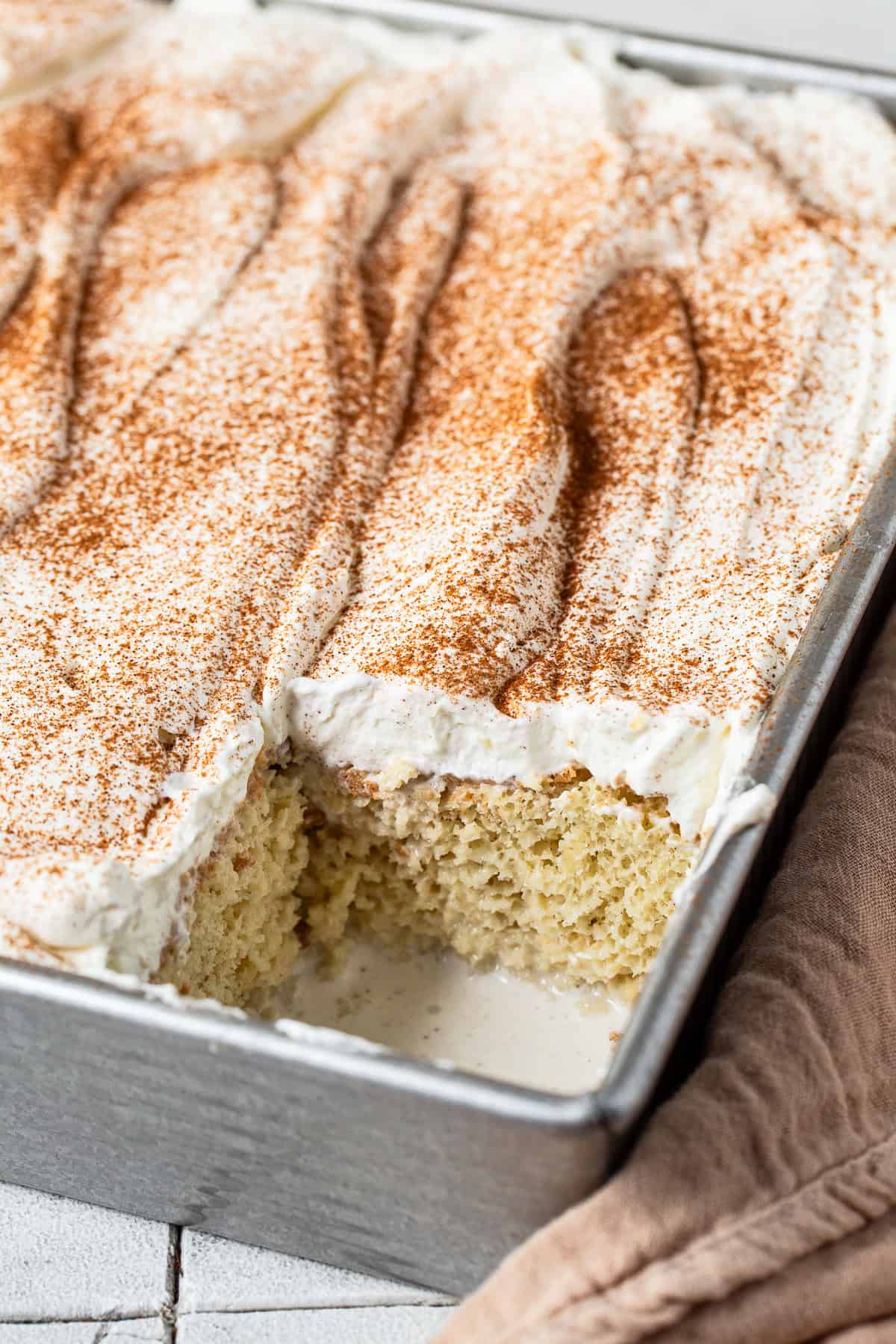 A tres leches cake in a pan with a slice taken out.