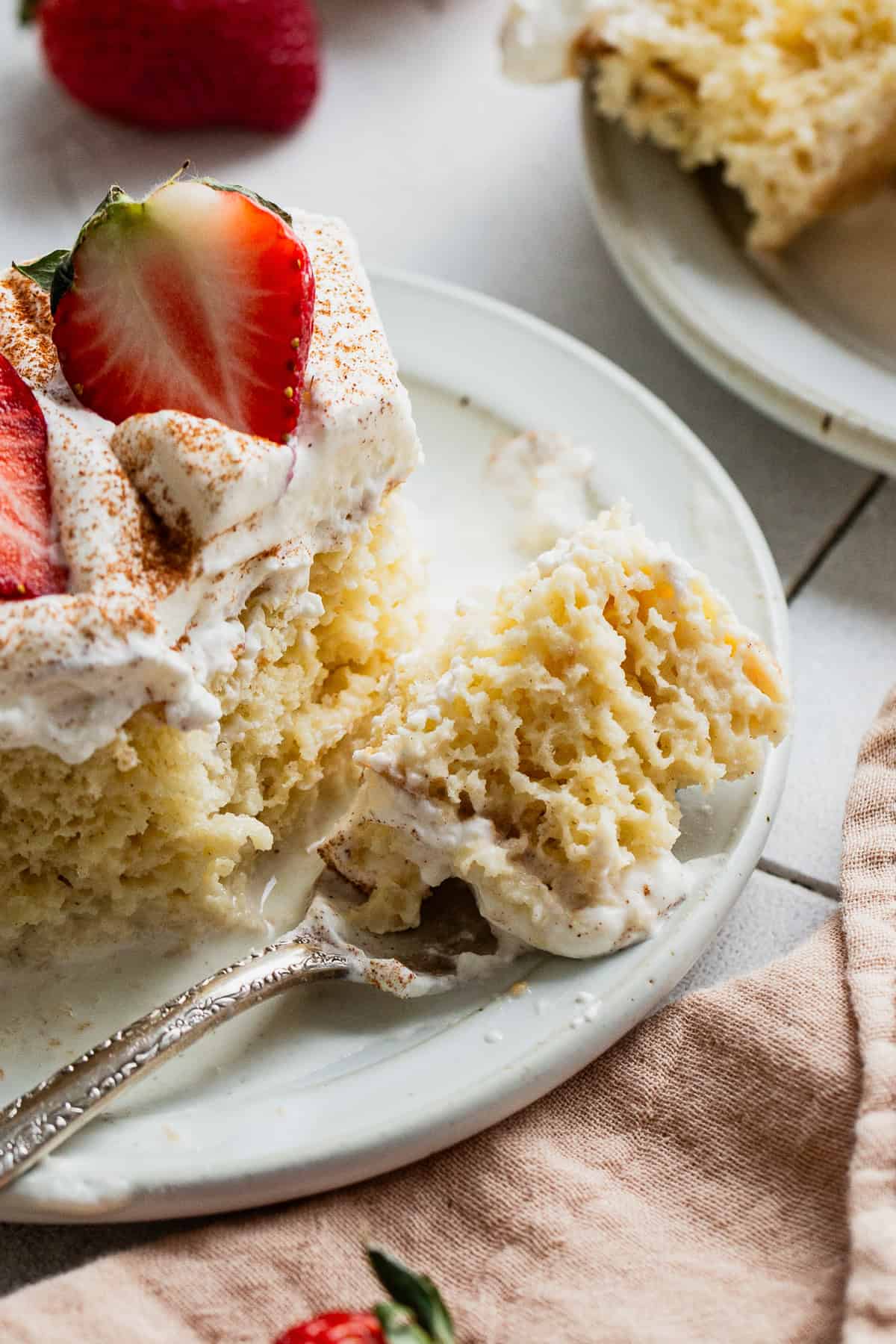 A bite of tres leches cake on a fork about to be eaten.